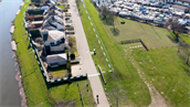 Deze afbeelding toont een luchtfoto van een woonwijk aan de rand van een waterweg, waarbij de nadruk ligt op de waterkering en beschermingsmaatregelen tegen overstromingen.