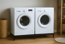 Een wasmachine en een droger staan zij-aan-zij op een zwart metalen frame, ter bescherming tegen wateroverlast.